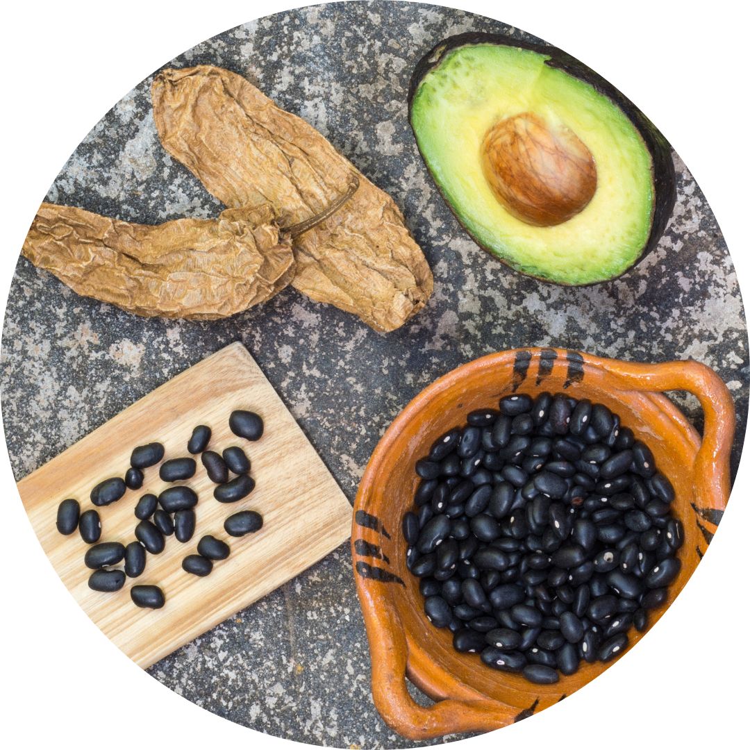 A cut avocado, black beans in a pot, and a brown root laid out together