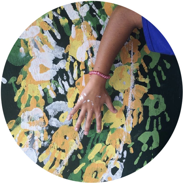 A child's hand on top of a painting of lots of hands