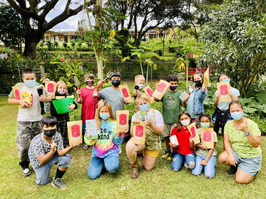 Youth Garden Grant A group of kids outside holding up seed packets and various other things