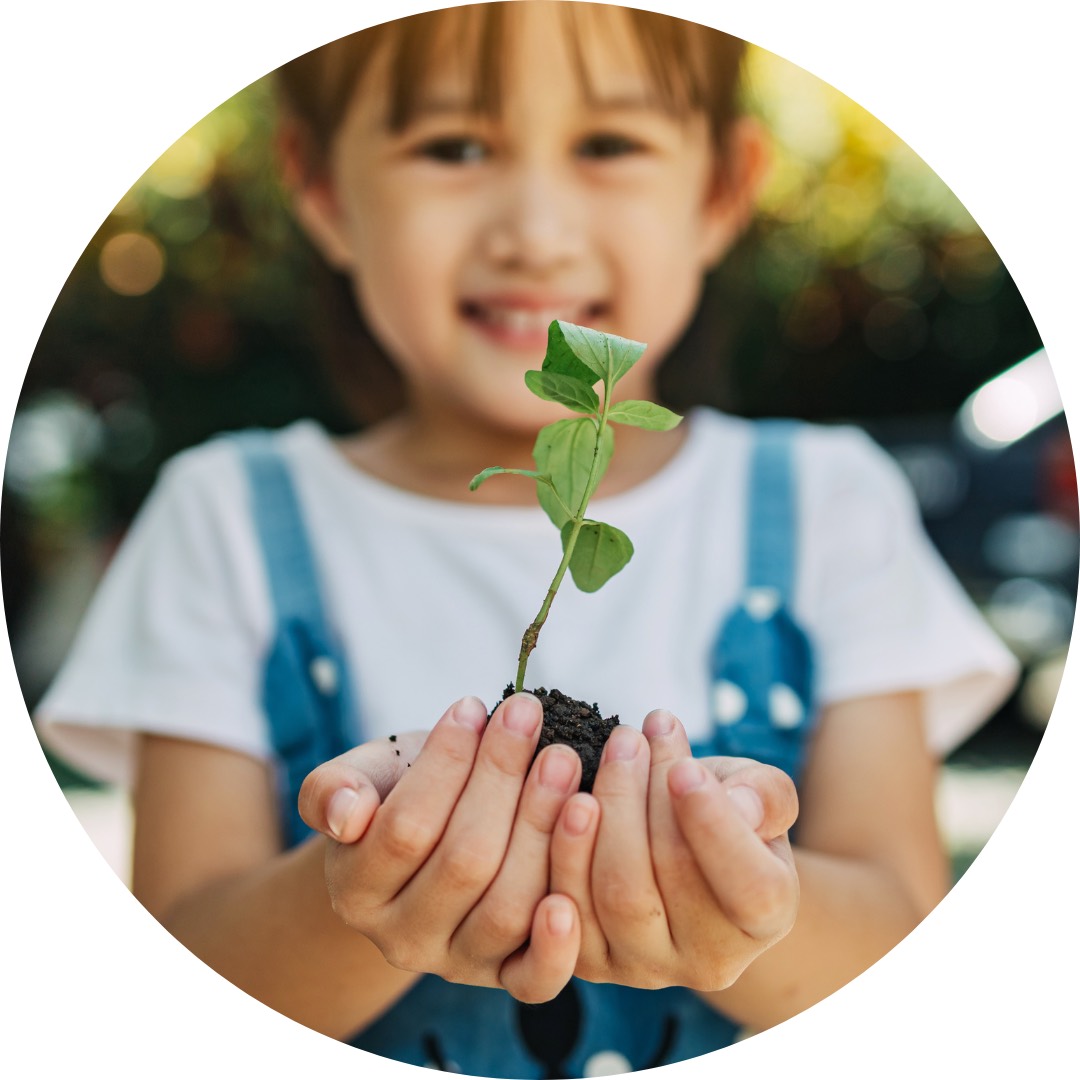A smiling child holds out a seedling.