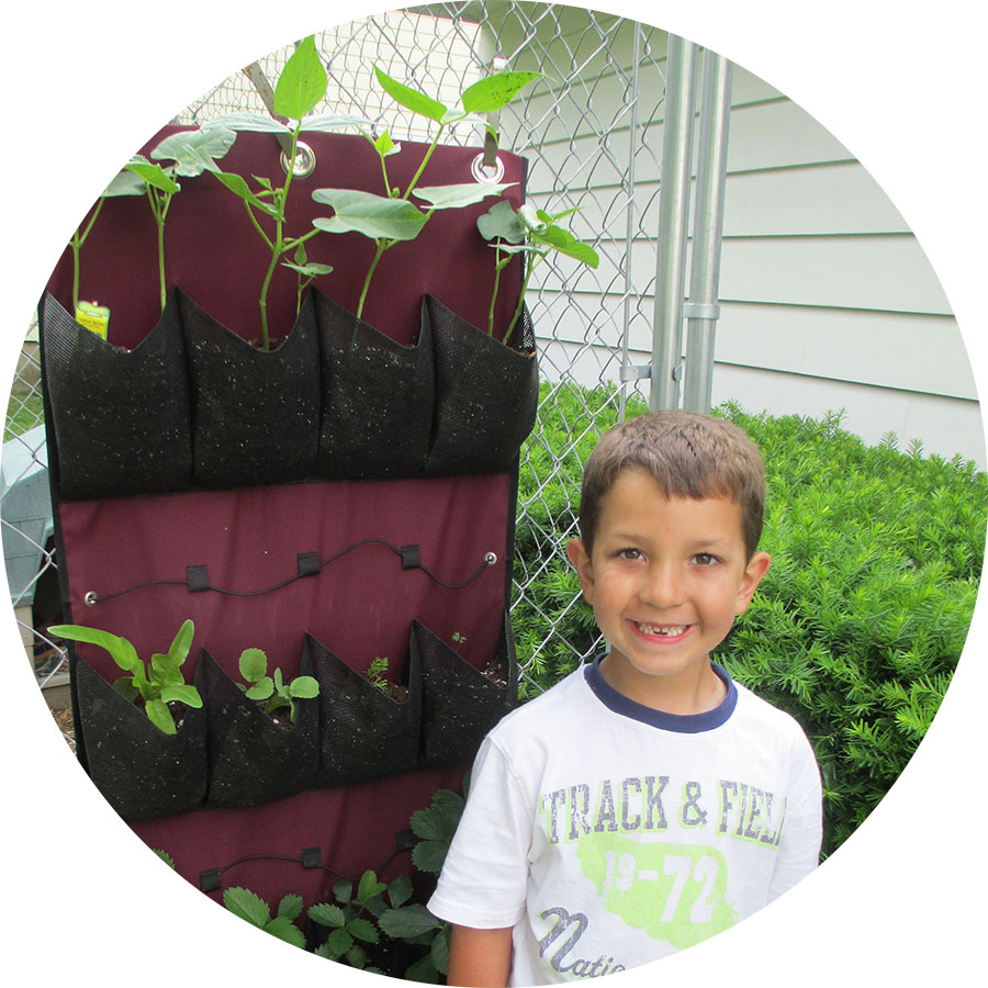 A child stands in front of a vertical shoe organizer that is planted with soil and plants.