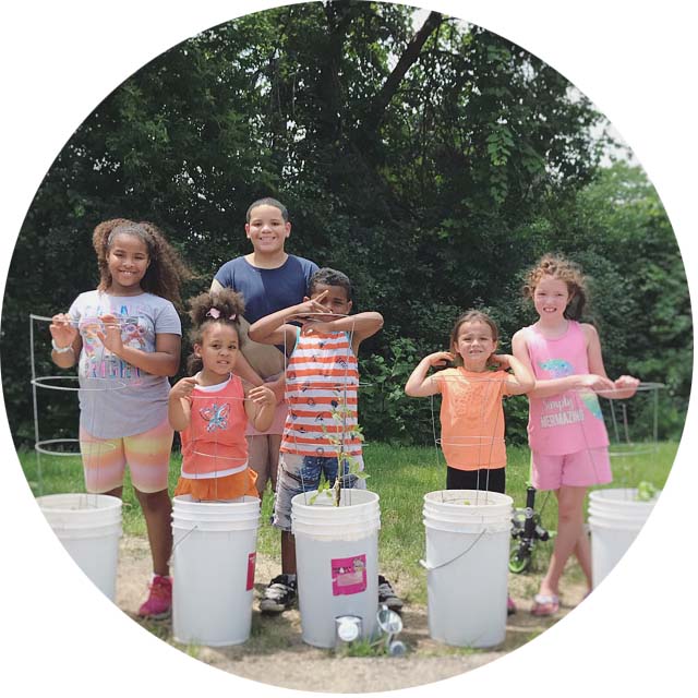 Six kids standing in front of a garden made of 5-gallon white buckets