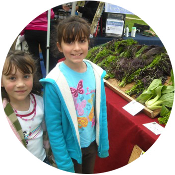 Two young girls at a farmers market looking at a lettuce stand