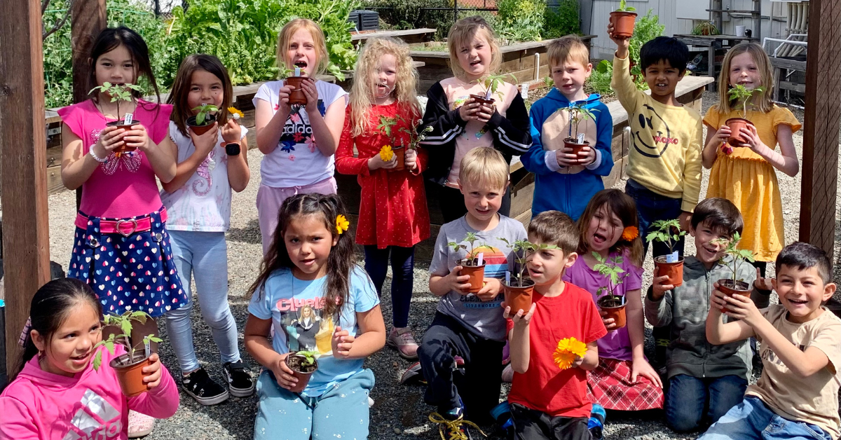 Lots of kids holding plants in pots and looking toward the camera.
