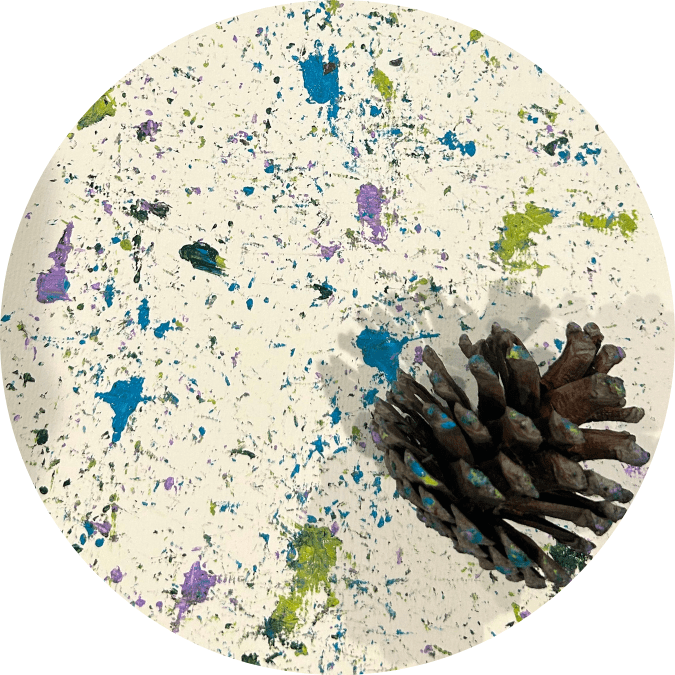 A purple, blue, and green splatterpaint with a pinecone nearby.