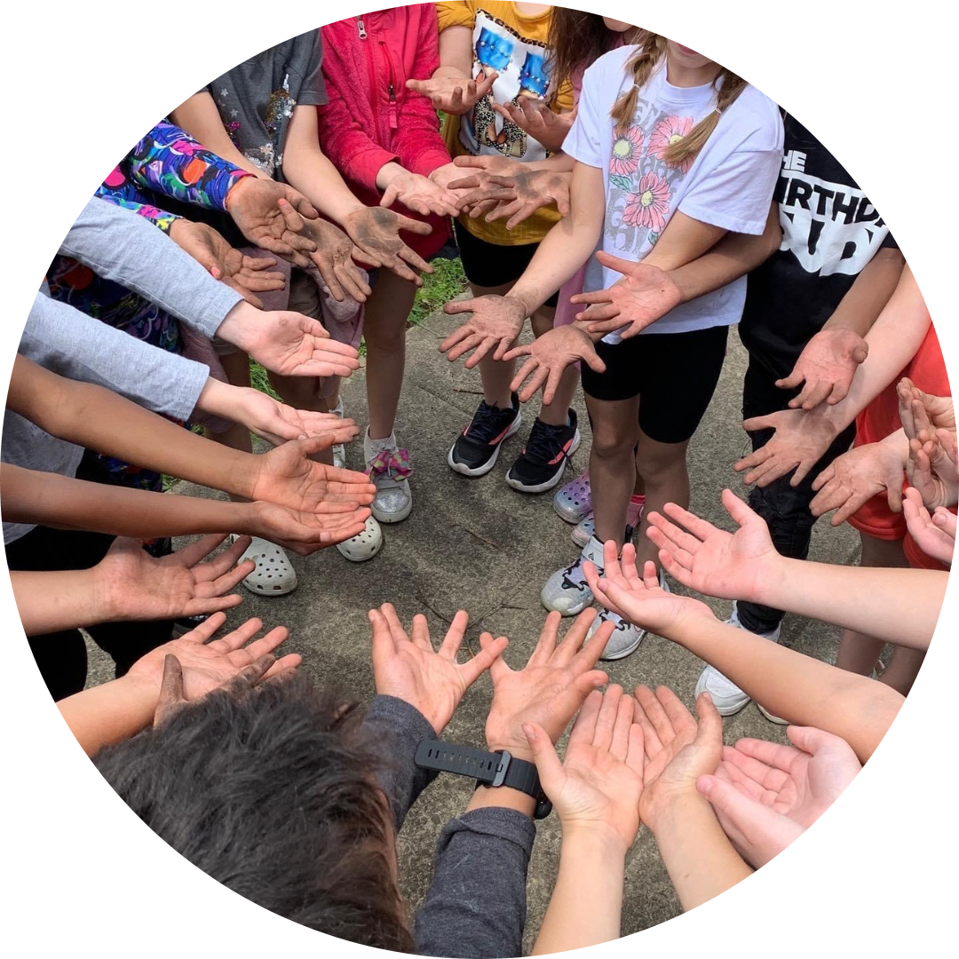 Kids in a circle with their hands in the middle. Only their arms are visible in the photo.