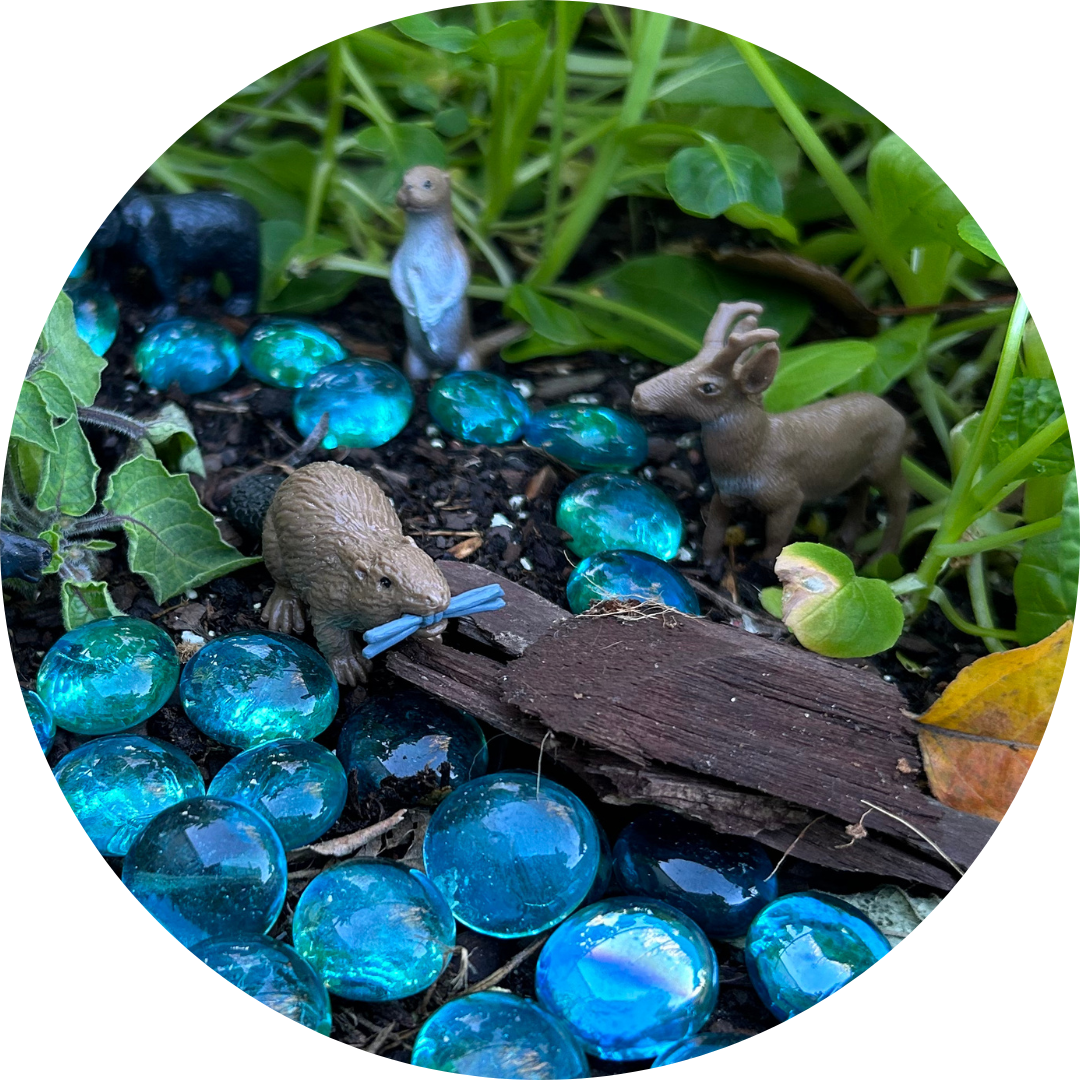 A miniature playscape of tiny animals, blue glass stones, and small green plants.